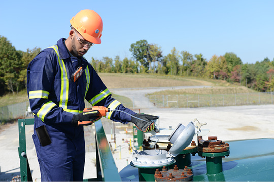 A lone worker uses a personal gas monitor with a sampling pump to take a reading inside a vat