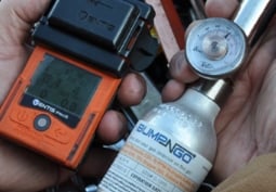Close-up of industrial worker bump testing a personal gas monitor with calibration gas