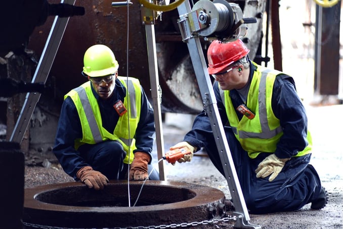 Two workers look down into a tank while taking a gas reading