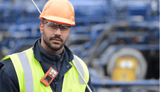 man wearing personal protective equipment and a personal gas detector on his collar looks forward