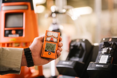 person hold personal gas detector in front of docking stations