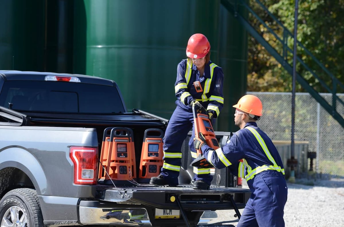 Two workers unload area gas monitors from the bed of a truck