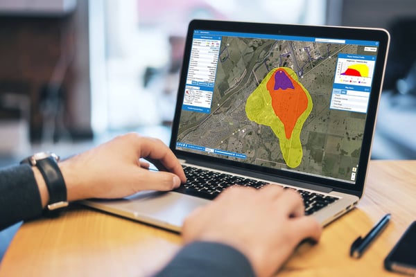 Over someone's shoulder, a laptop with a dynamic plume model shows predicted chemical leak spread over a map