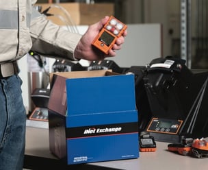 worker off-camera pulls a personal gas monitor out of a shipping box labeled, "iNet Exchange"