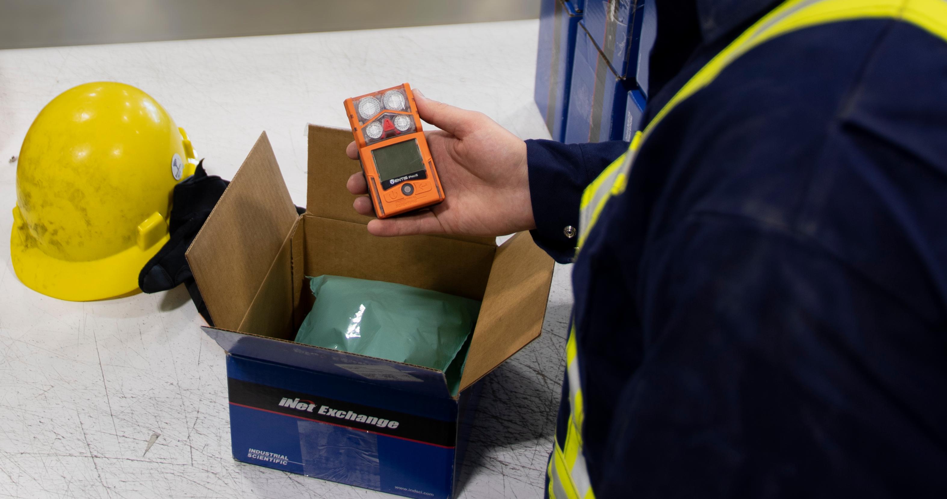 Someone pulls a personal gas monitor out of a shipping box marked "iNet Exchange"