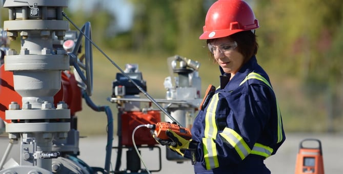 A lone worker wearing personal protective equipment takes a gas reading using sample tubing and a hand-held gas monitor