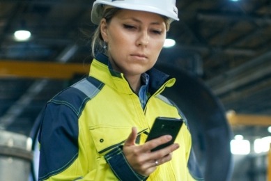 woman in work uniform and hardhat looks down at cell phone