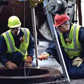 Two workers using confined space monitors to test a confined space